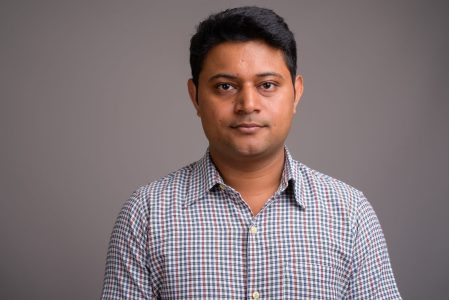 Studio shot of young Indian businessman wearing checkered shirt against gray background